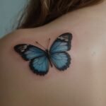 Tatuagem de borboleta azul em estilo micro realismo 3D no ombro de uma mulher, com detalhes vibrantes nas asas.
