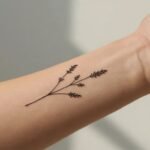 Tatuagem feminina delicada no antebraço com desenho de flores silvestres e lavanda em estilo traço fino (fine line).