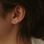Tatuagem minimalista pequena de lua e estrelas feita atrás da orelha, estilo discreto e feminino. Tatuagens femininas.